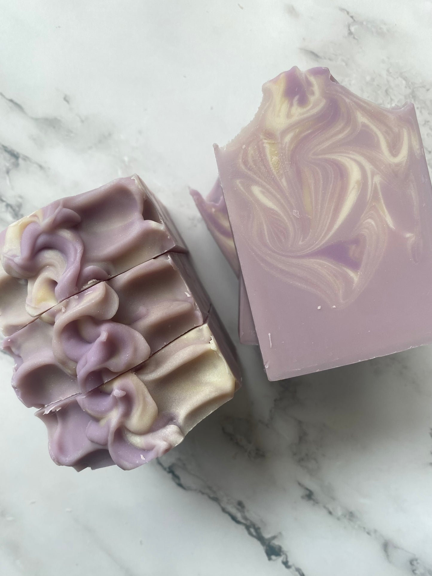 Image of purple, white, and tan swirled soap bars with 3 bars stacked on top of one another and 3 bars standing vertically photographed on a white marble background.
