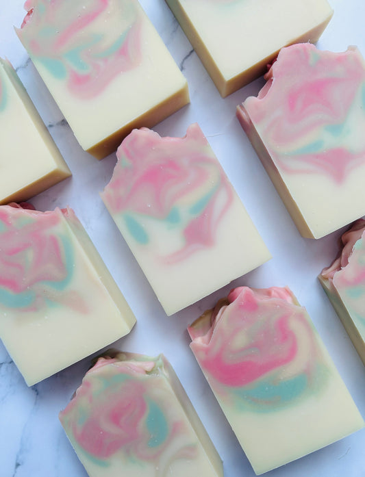 Image of 9 pink, green, and gold swirled soap bars photographed vertically on a white marble background.