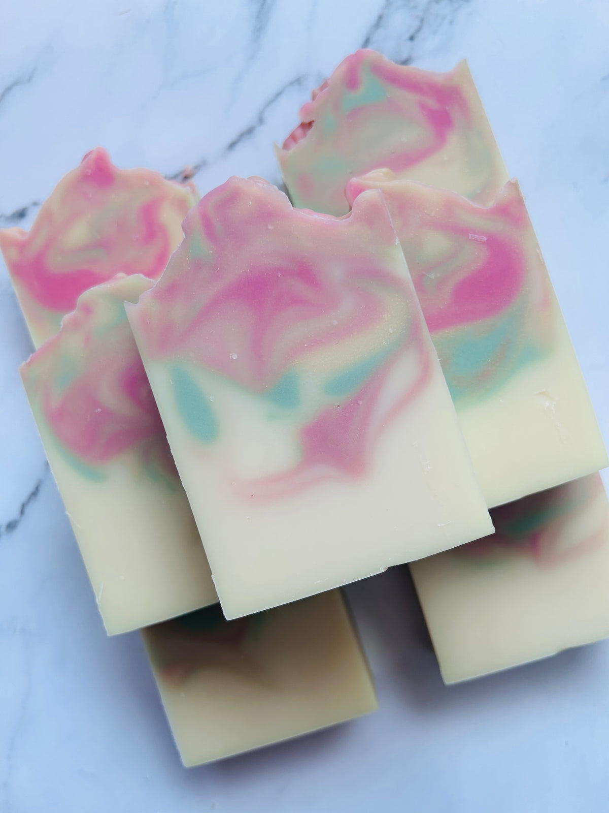 Image of 7 pink, green, and gold swirled soap bars stacked on top of one another photographed on a white marble background.