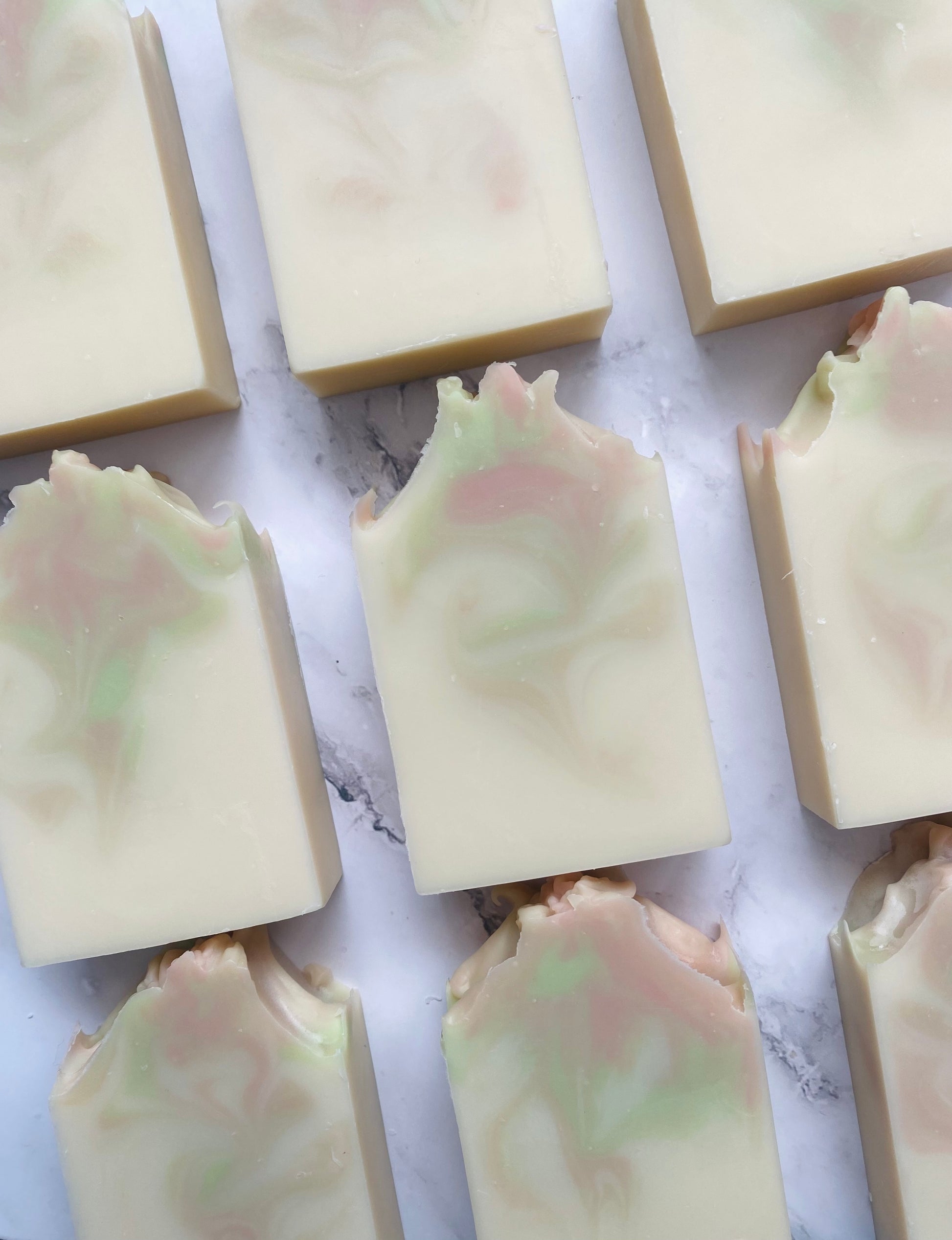 Image of 9 white, pink, and green swirled soap bars photographed vertically on a white marble background.