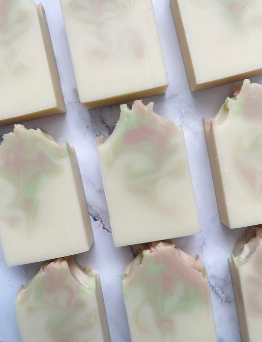Image of 9 white, pink, and green swirled soap bars photographed vertically on a white marble background.