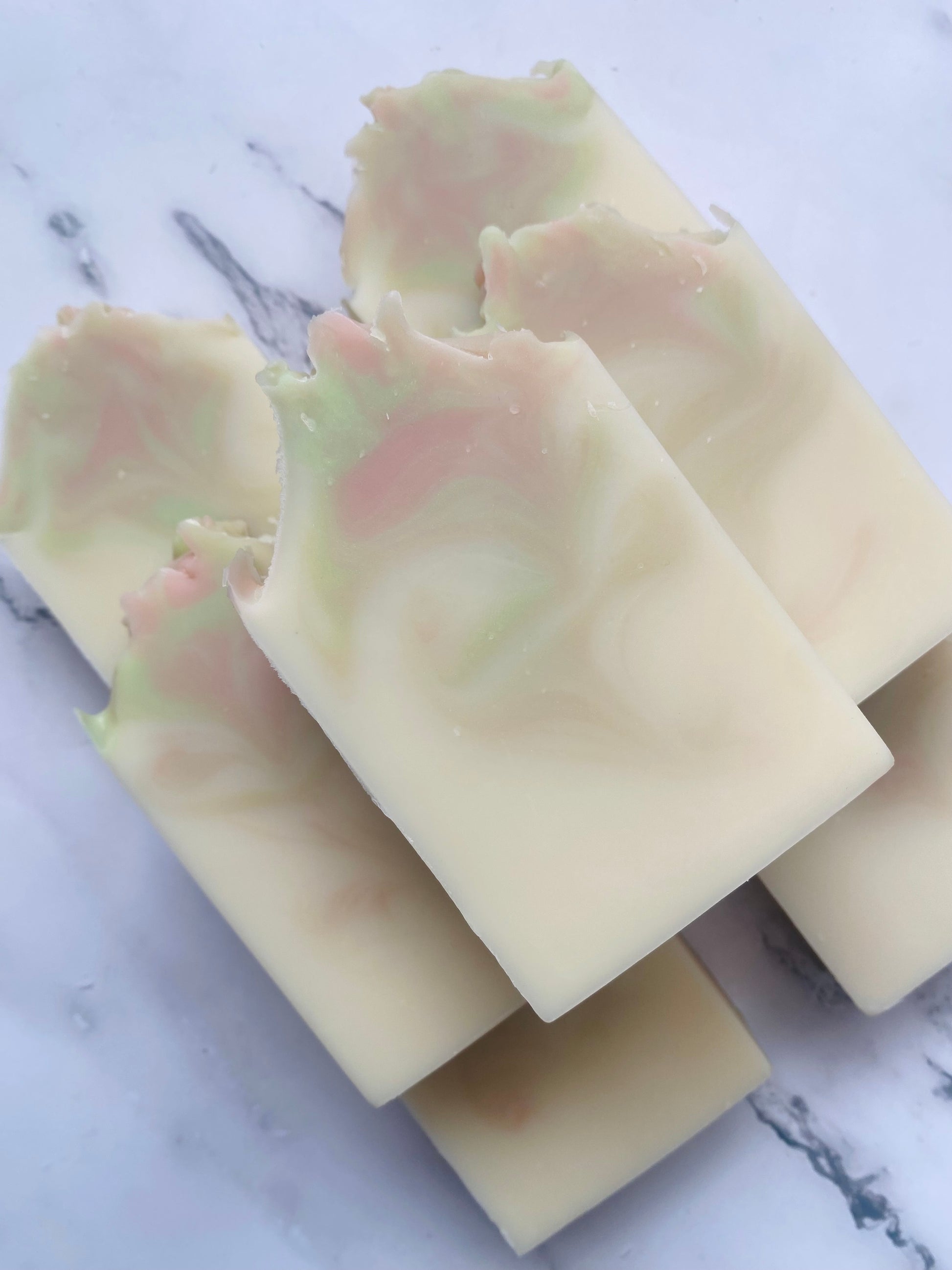 Image of 7 white, pink, and green swirled soap bars stacked on top of one another photographed on a white marble background.