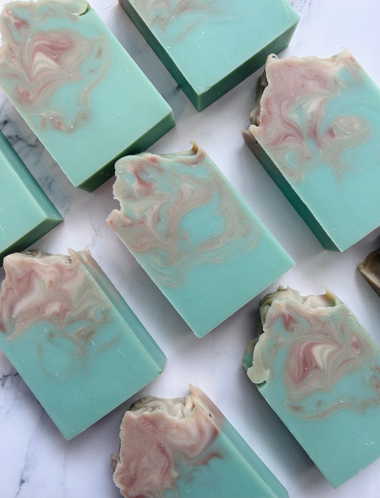 Image of 9 teal, brown, and white swirled soap bars photographed vertically on a white marble background.