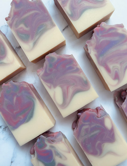 Image of 9 purple, pink, and gray swirled soap bars photographed vertically on a white marble background.