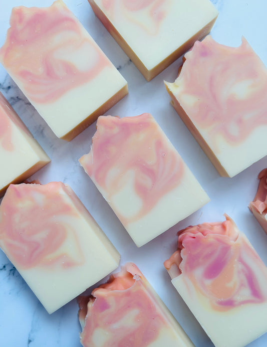 Image of 9 pink, orange, and yellow swirled soap bars photographed vertically on a white marble background.