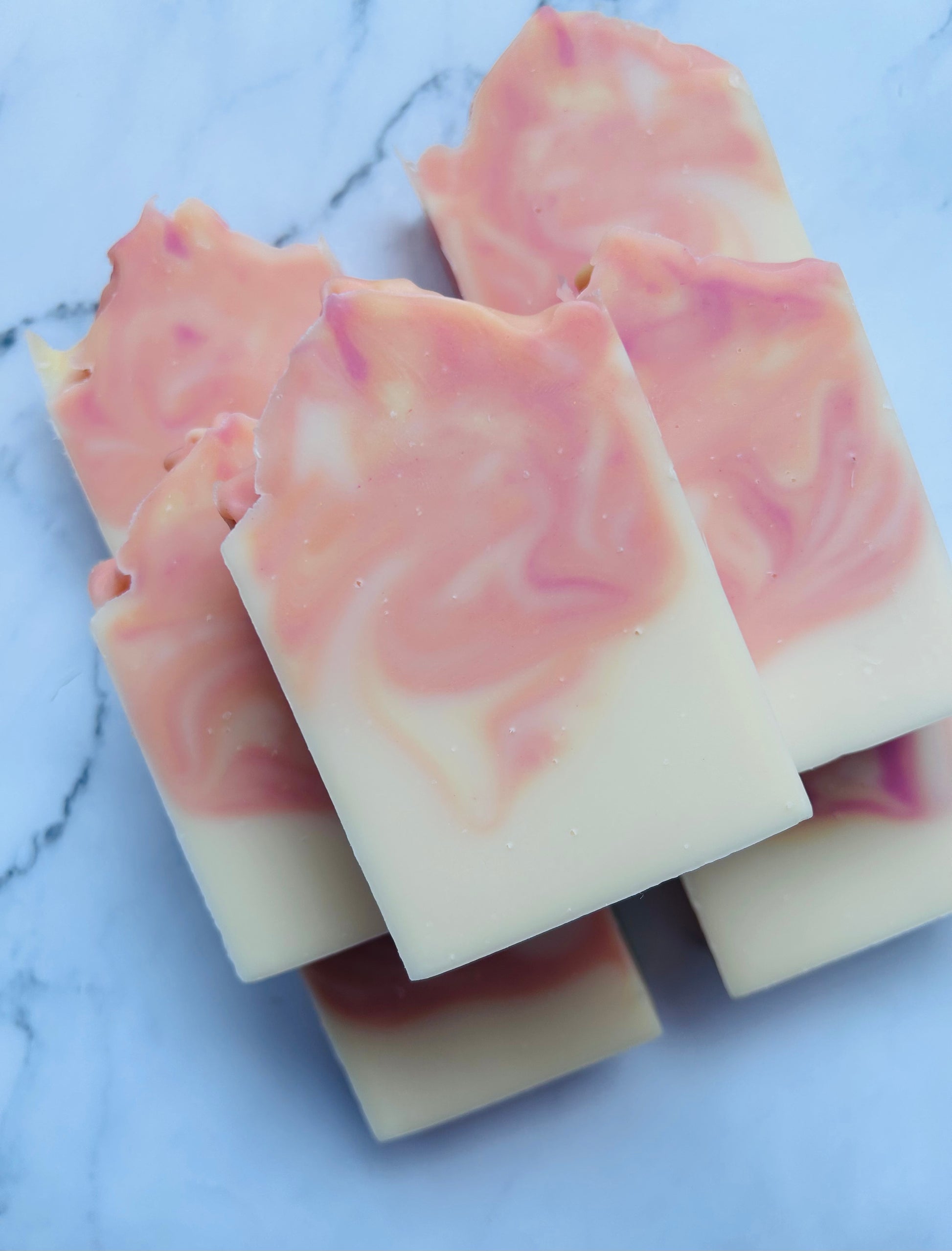 Image of 7 pink, orange, and yellow swirled soap bars stacked on top of one another photographed on a white marble background.