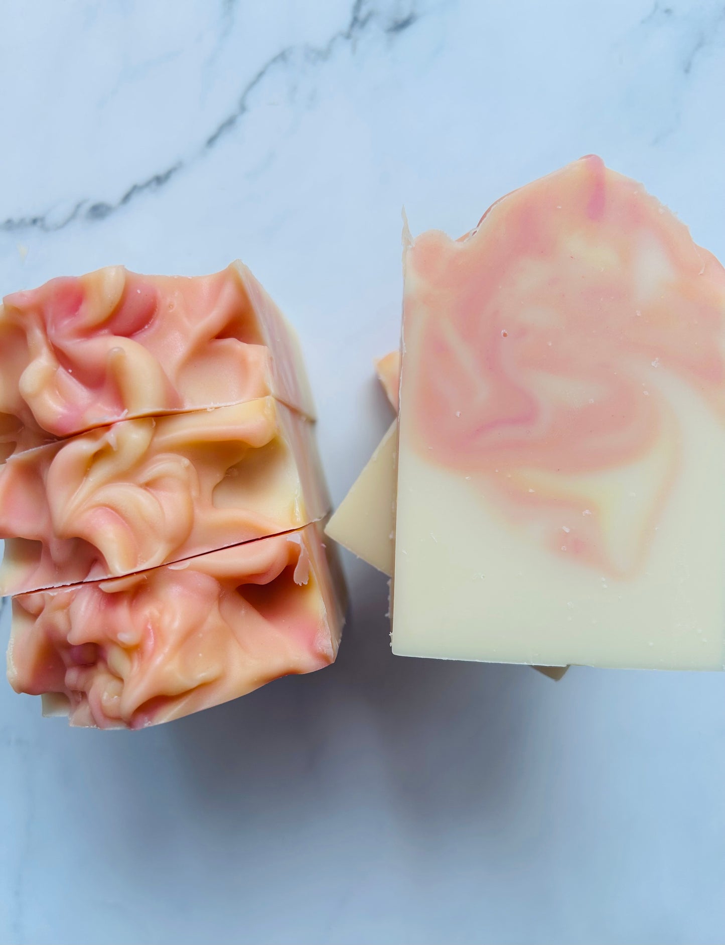 Image of pink, orange, and yellow swirled soap bars with 3 bars stacked on top of one another and 3 bars standing vertically photographed on a white marble background.