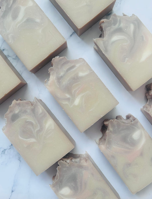 Image of 9 purple, white, and tan swirled soap bars photographed vertically on a white marble background.