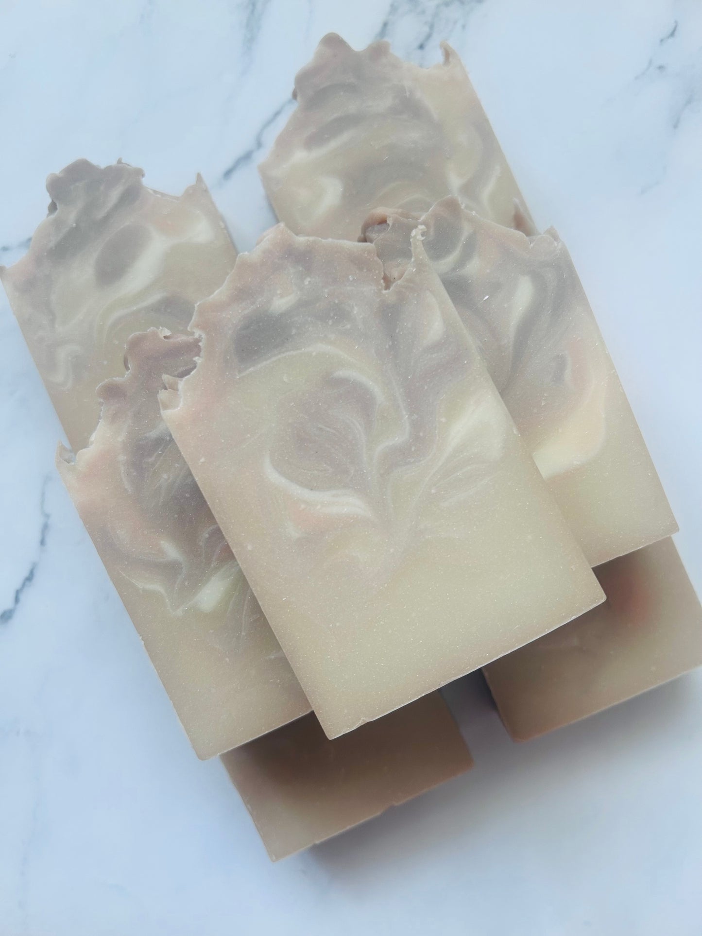Image of 7 purple, white, and tan swirled soap bars stacked on top of one another photographed on a white marble background.