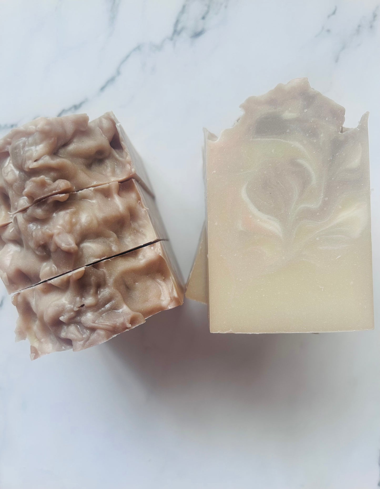 Image of purple, white, and tan swirled soap bars with 3 bars stacked on top of one another and 3 bars standing vertically photographed on a white marble background.