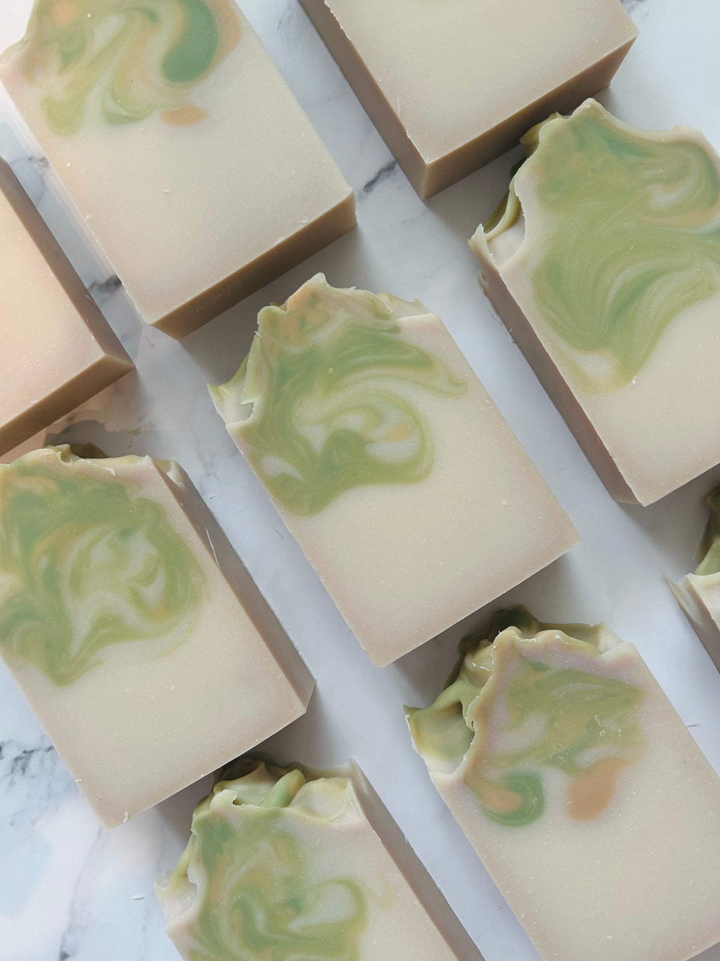 Image of 9 white, green, and gold swirled soap bars photographed vertically on a white marble background.