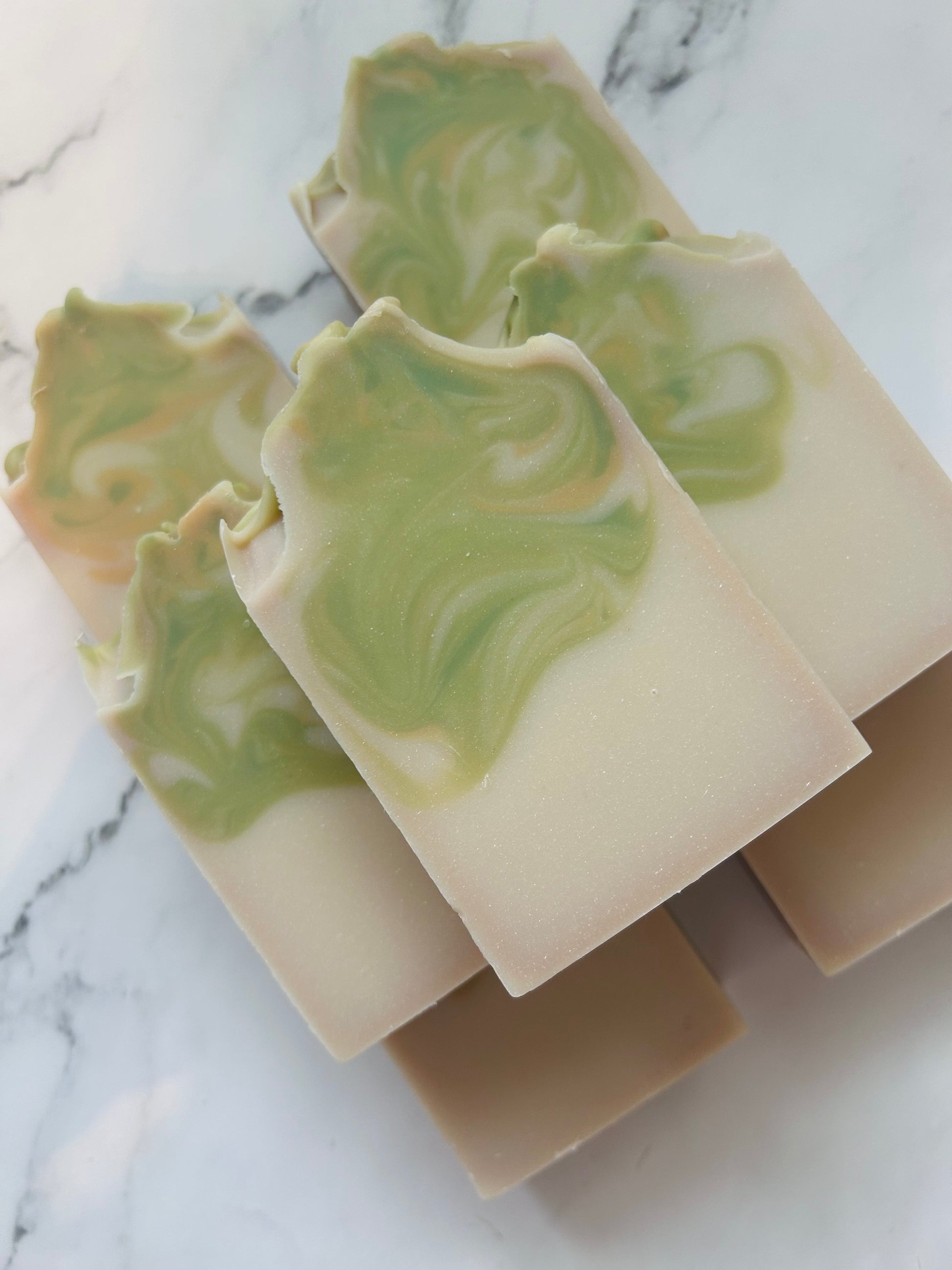 Image of 7 white, green, and gold swirled soap bars stacked on top of one another photographed on a white marble background.