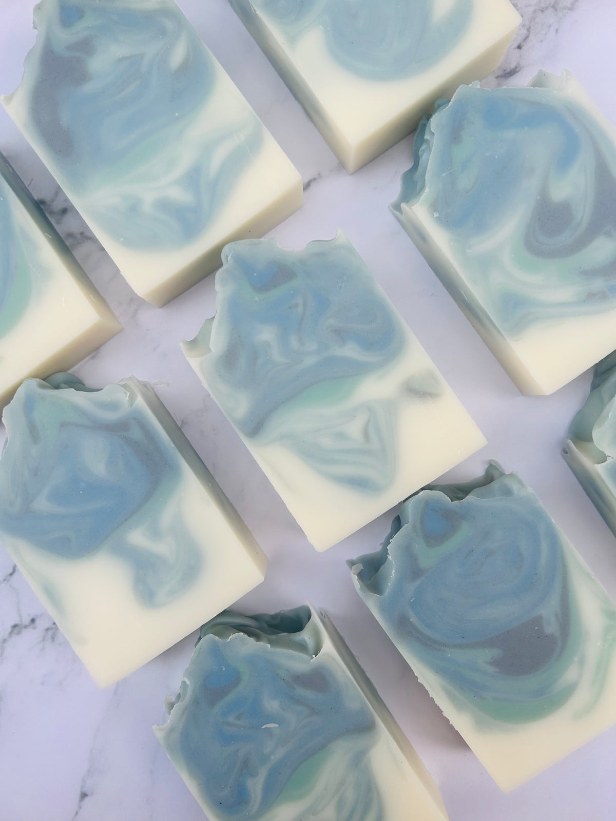 Image of 9 blue, green, and white swirled soap bars photographed vertically on a white marble background.