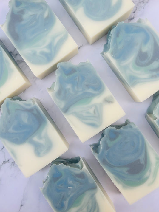 Image of 9 blue, green, and white swirled soap bars photographed vertically on a white marble background.