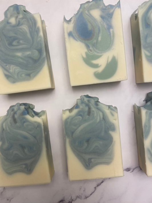 Image of 6 green, blue, and white swirled soaps photographed vertically against a white marble background.