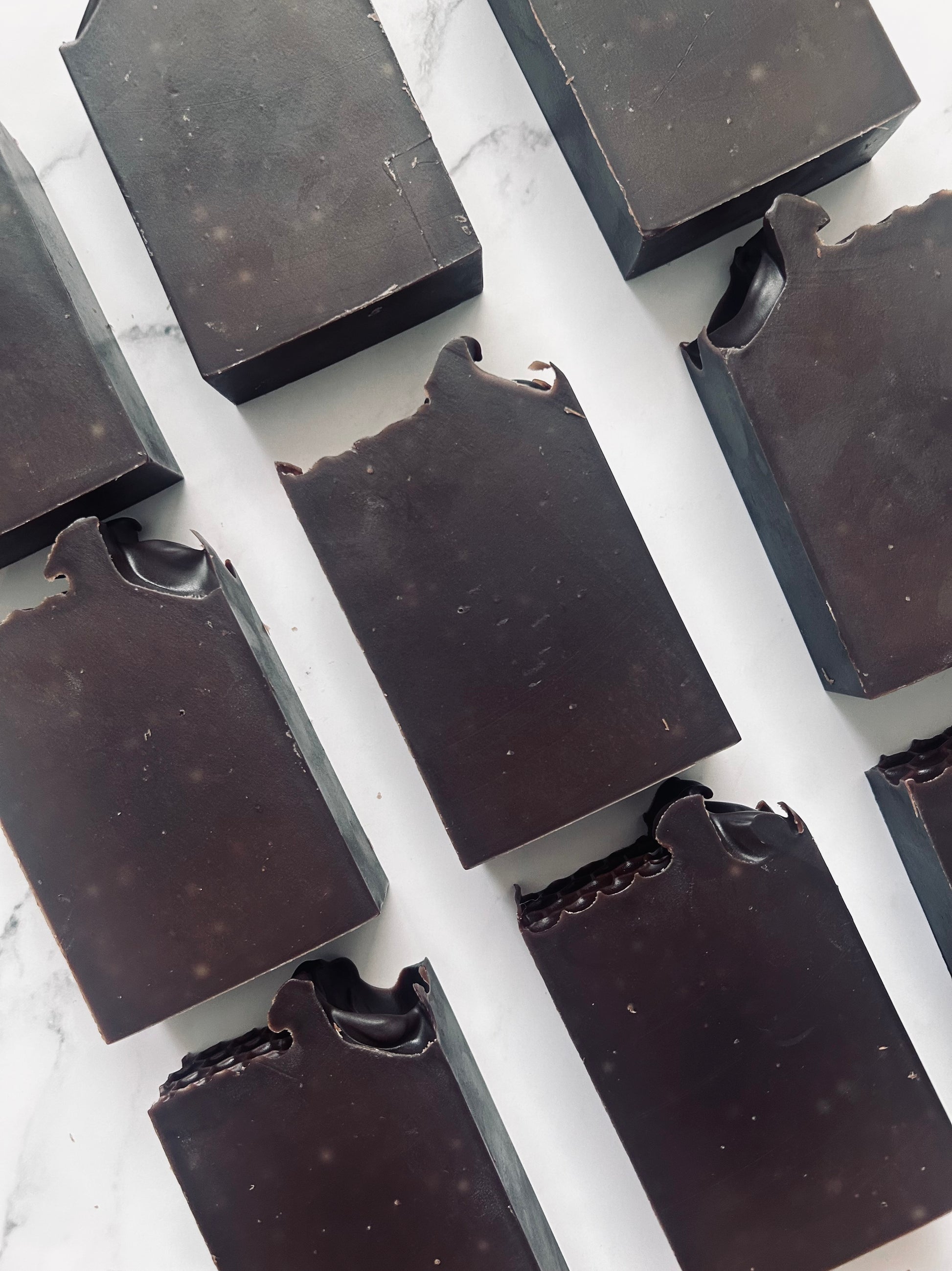 Image of 9 dark brown soap bars photographed vertically on a white marble background.