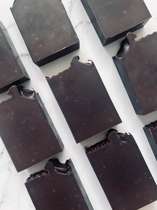 Image of 9 dark brown soap bars photographed vertically on a white marble background.
