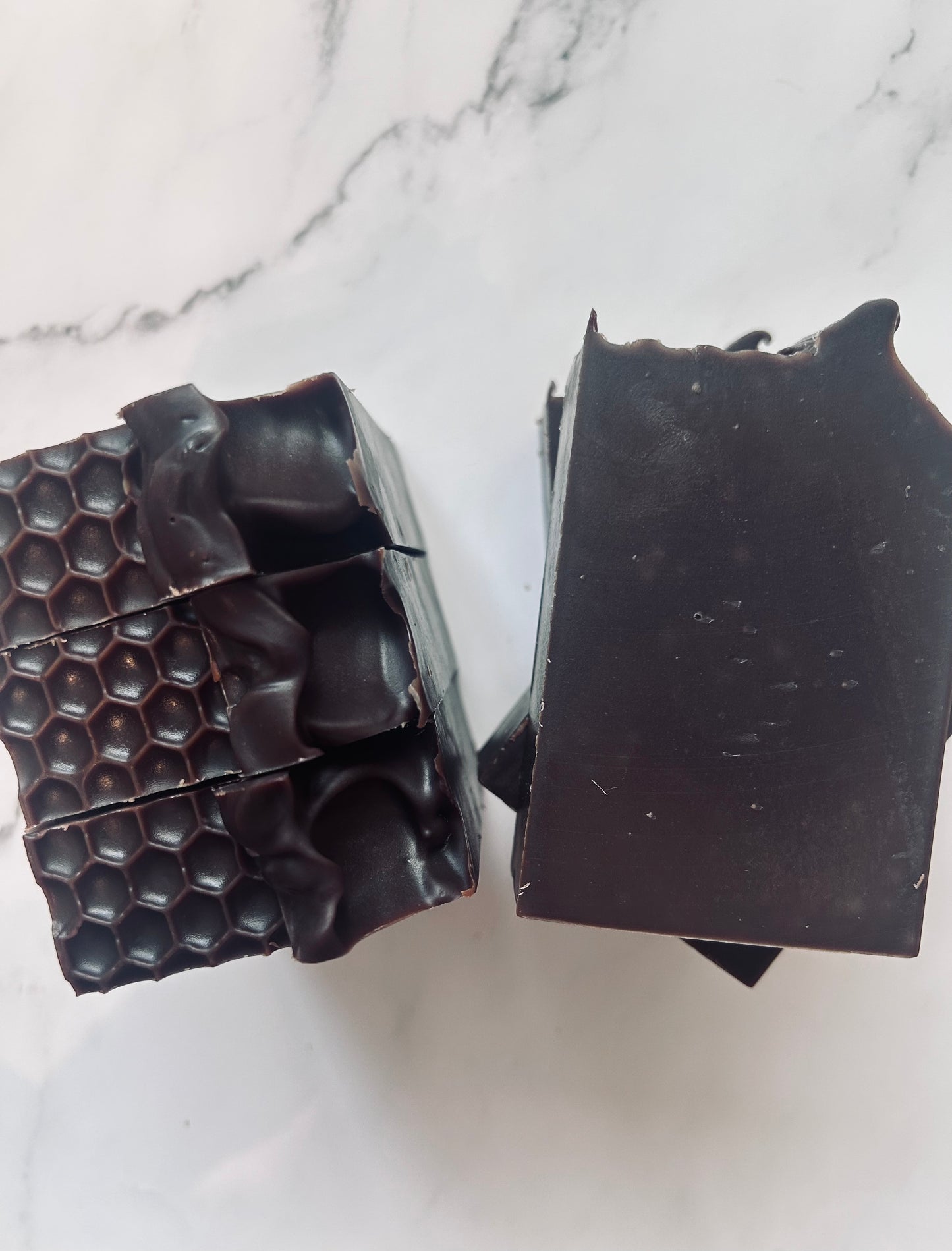 Image of dark brown soap bars with 3 bars stacked on top of one another and 3 bars standing vertically photographed on a white marble background.