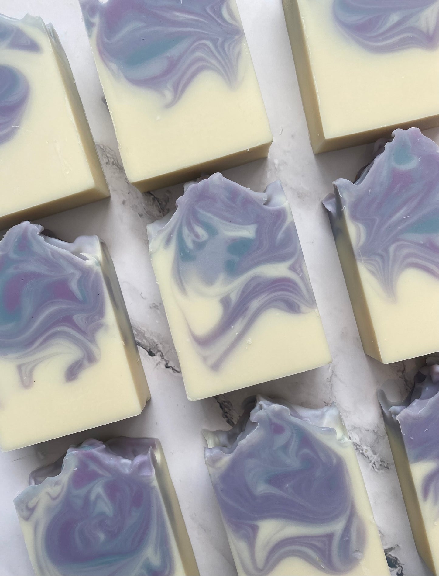 Image of 9 white, purple, and blue swirled soap bars photographed vertically on a white marble background.