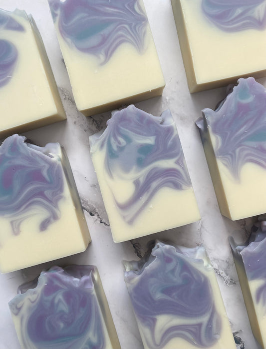 Image of 9 white, purple, and blue swirled soap bars photographed vertically on a white marble background.