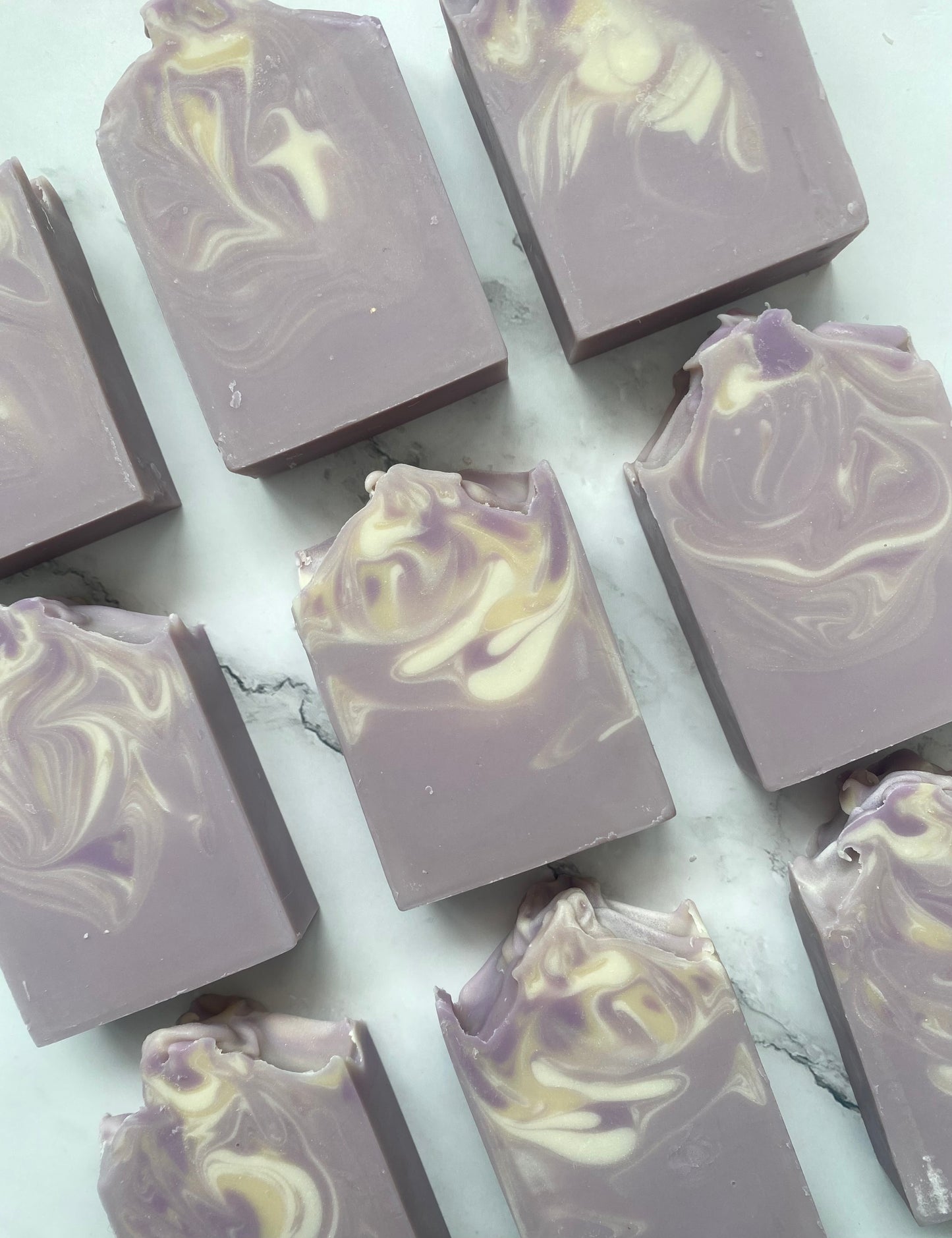 Image of 9 purple soap bars with white and tan swirls photographed vertically on a white marble background.