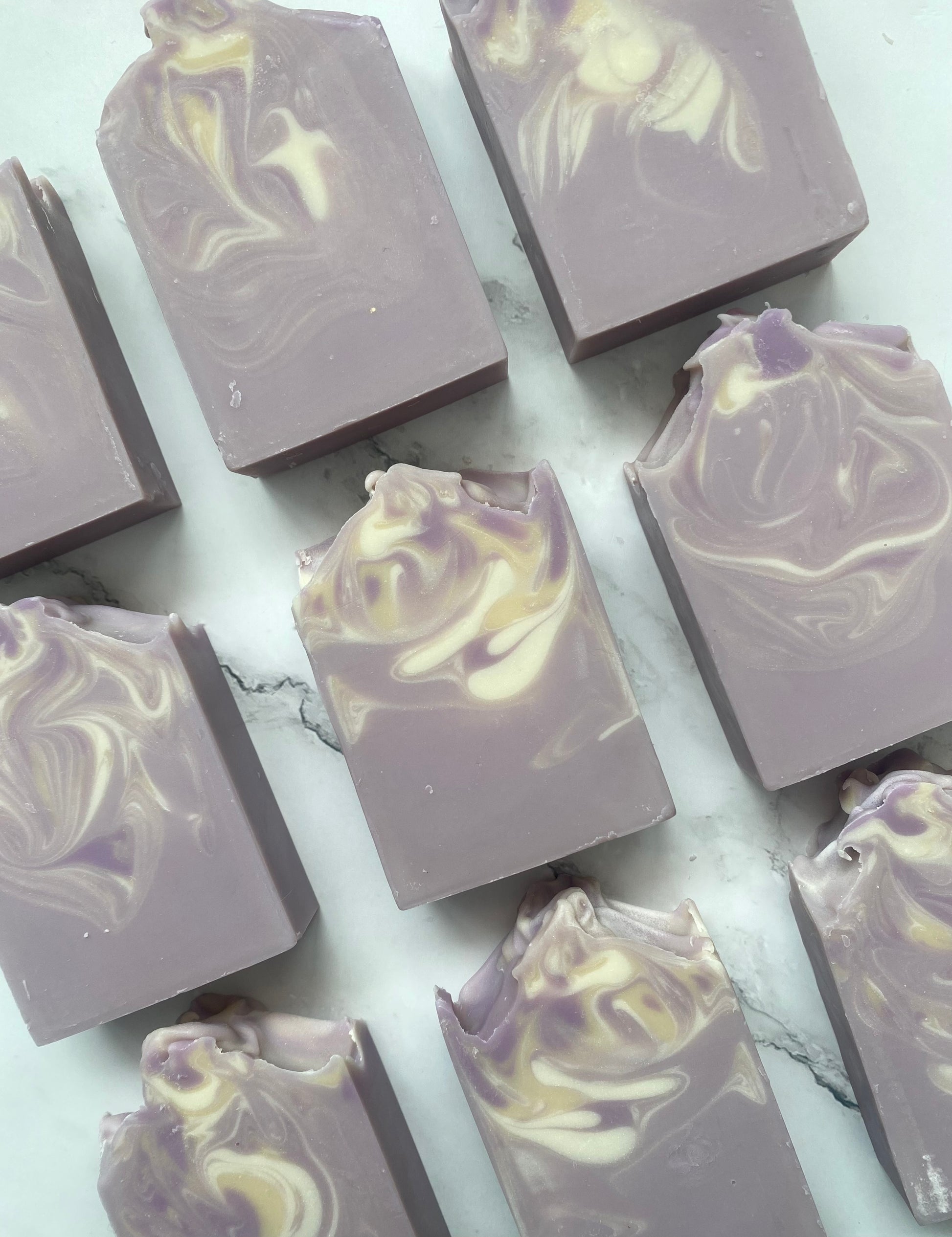 Image of 9 purple soap bars with white and tan swirls photographed vertically on a white marble background.