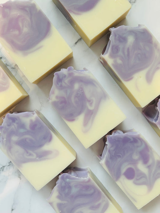 Image of 9 white and purple swirled soap bars photographed vertically on a white marble background.