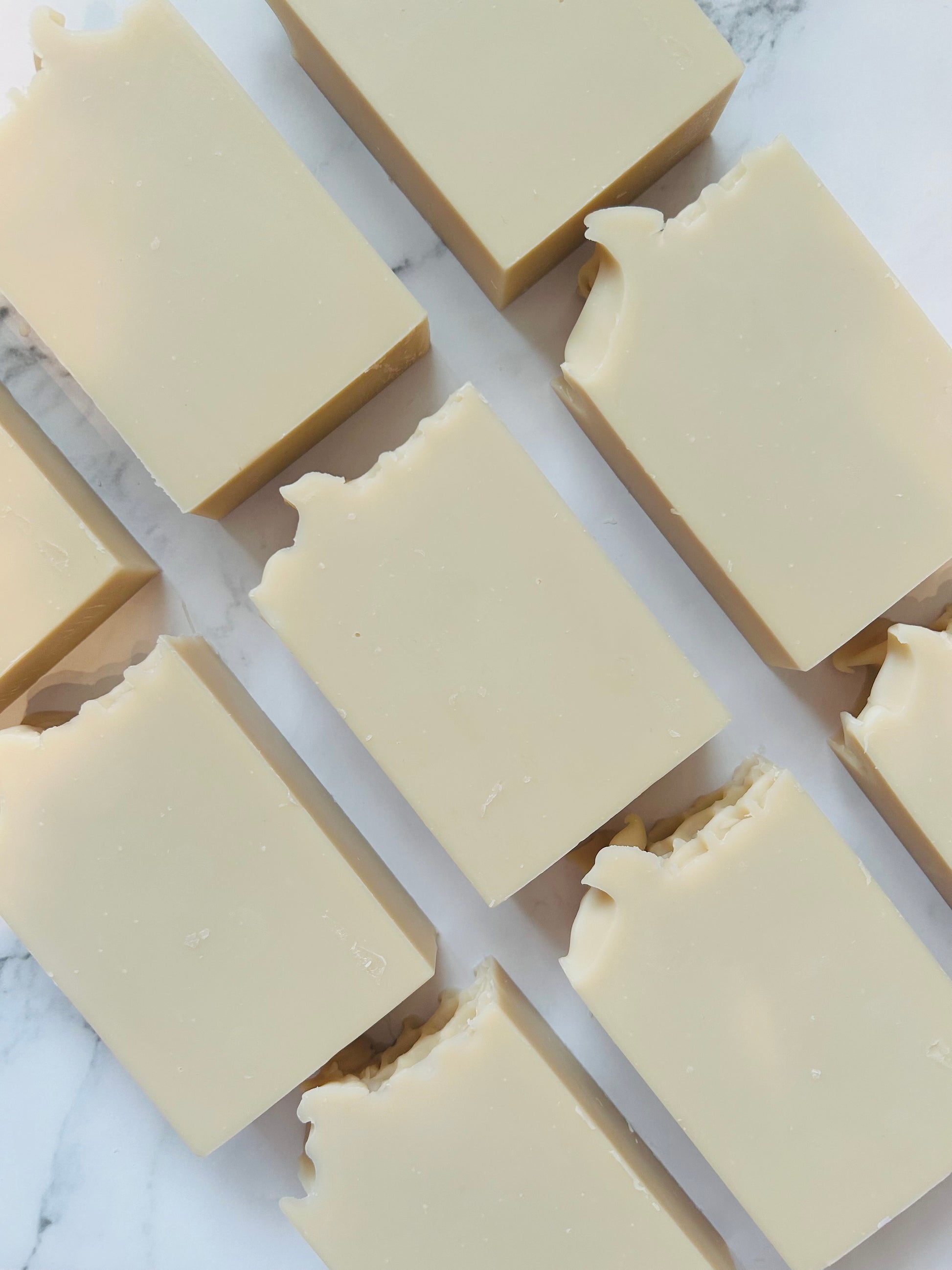 Image of 9 cream colored soap bars photographed vertically on a white marble background.