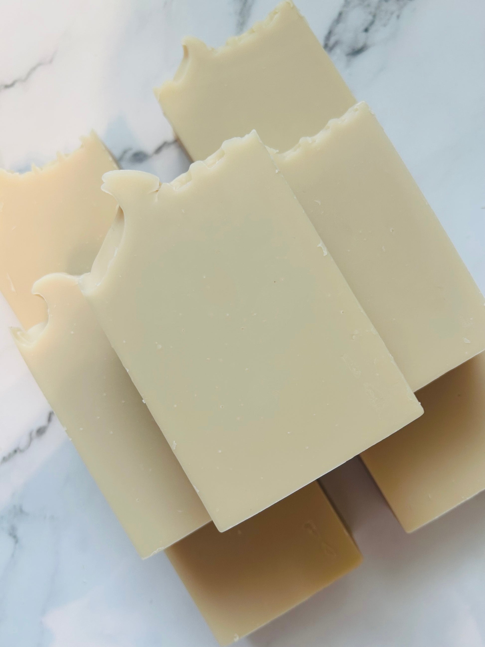 Image of 7 cream colored soap bars stacked on top of one another photographed on a white marble background.