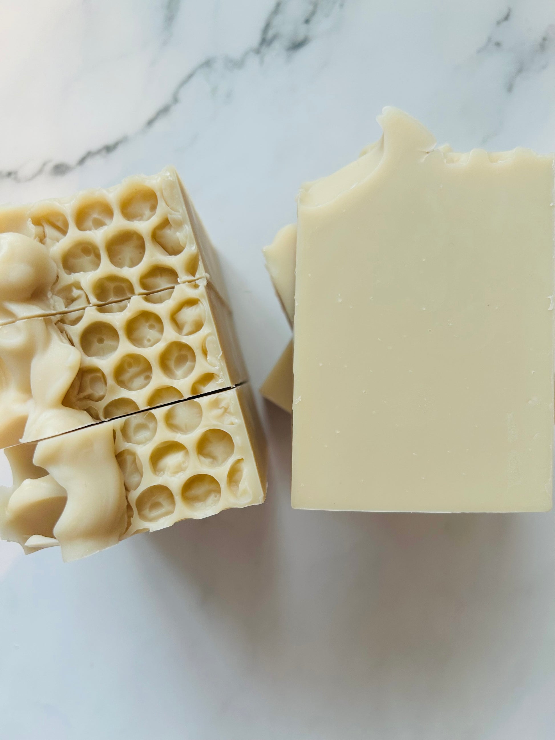Image of cream colored soap bars with 3 bars stacked on top of one another and 3 bars standing vertically photographed on a white marble background.