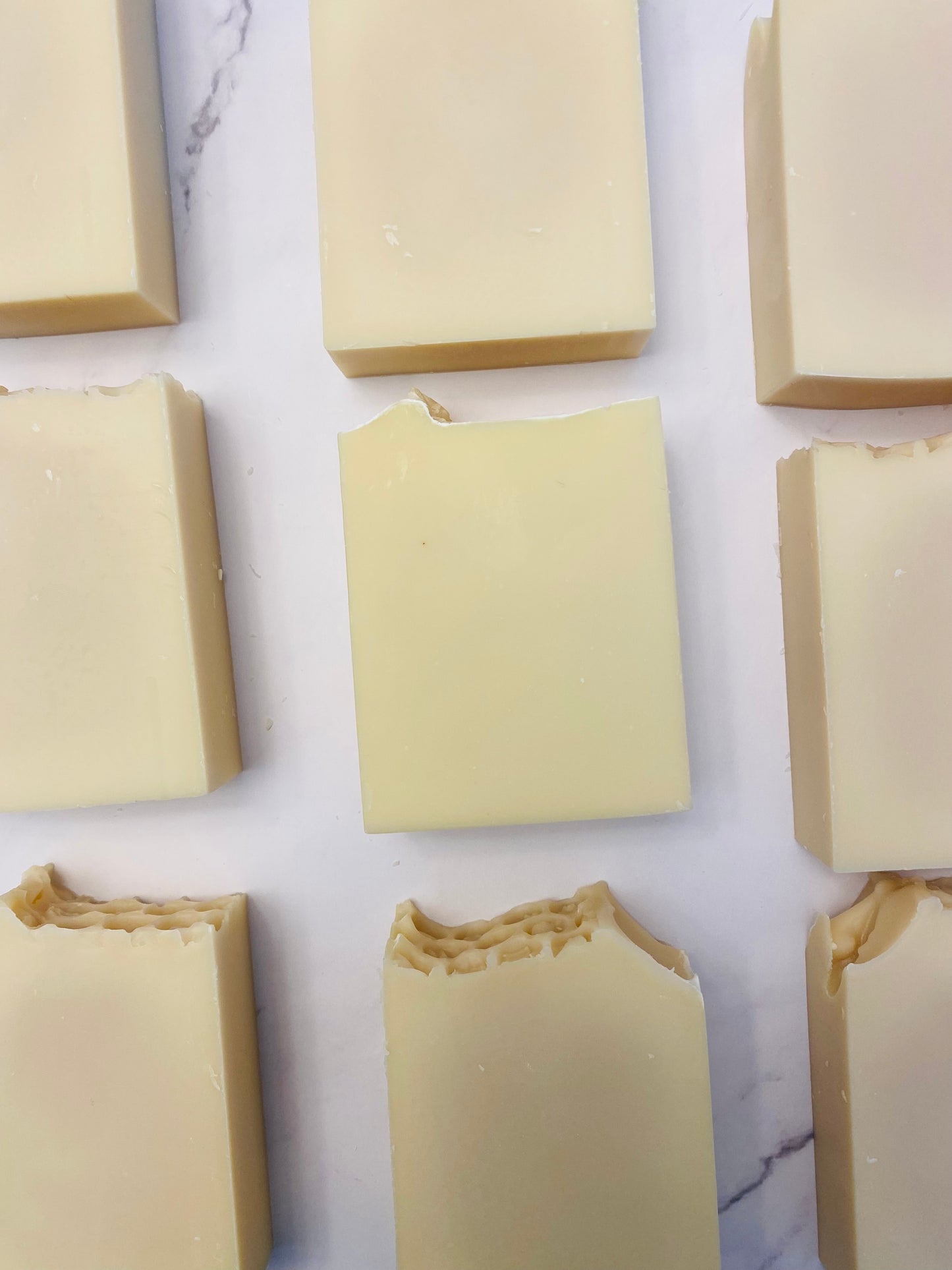 Image of 9 cream colored soap bars photographed vertically on a white marble background.