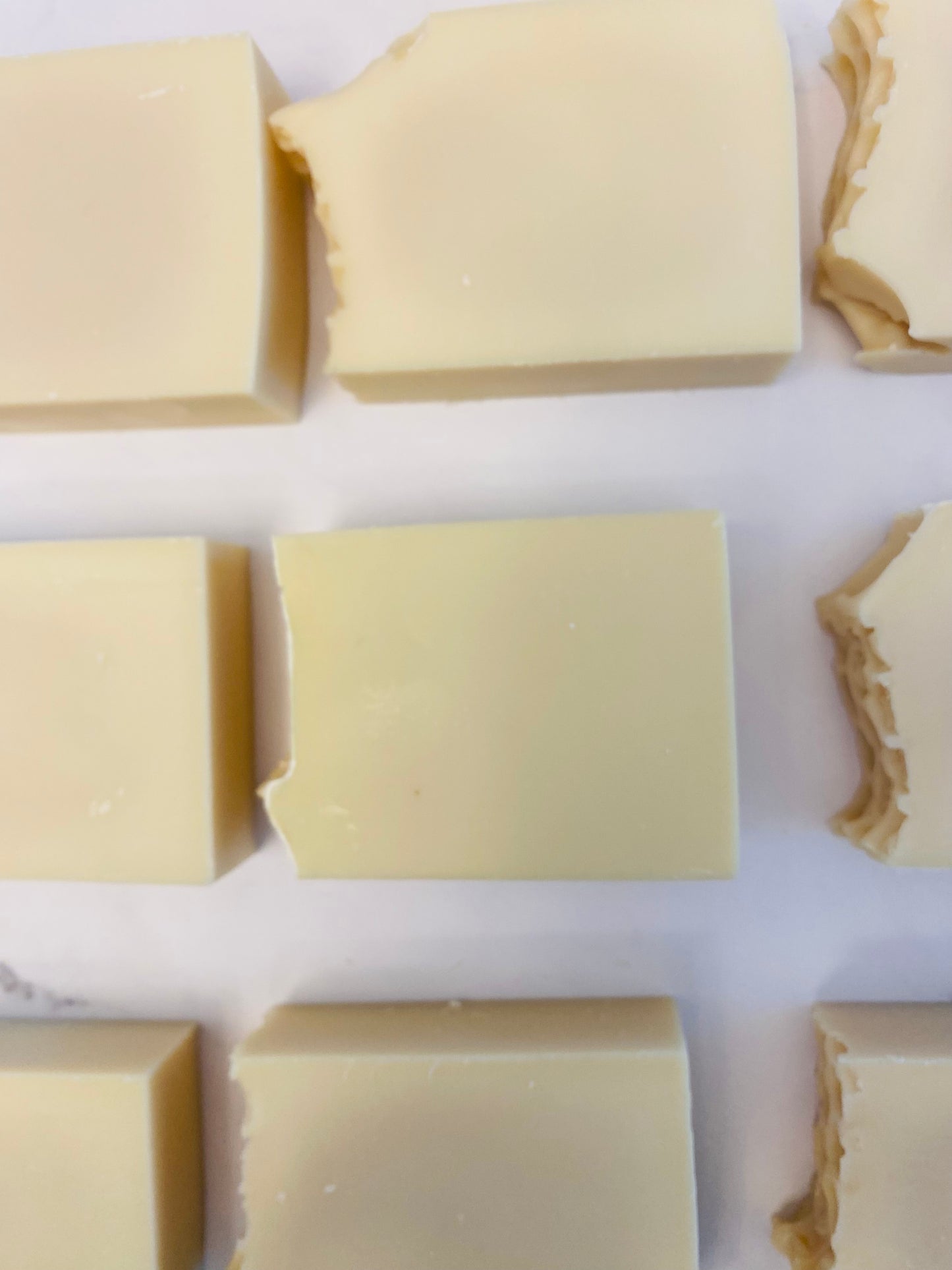 Image of 9 cream colored soap bars photographed horizontally on a white marble background.