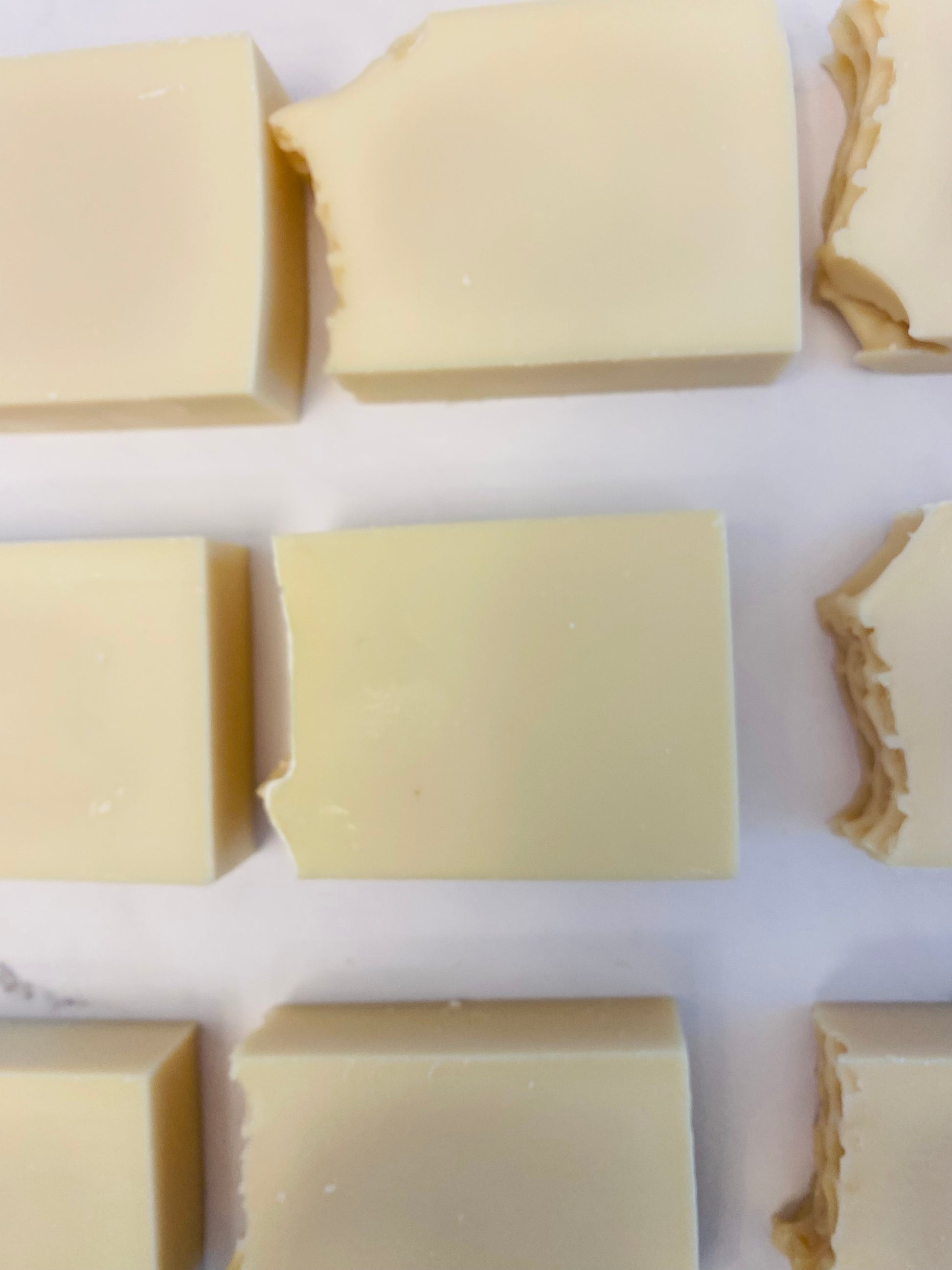 Image of 9 cream colored soap bars photographed horizontally on a white marble background.