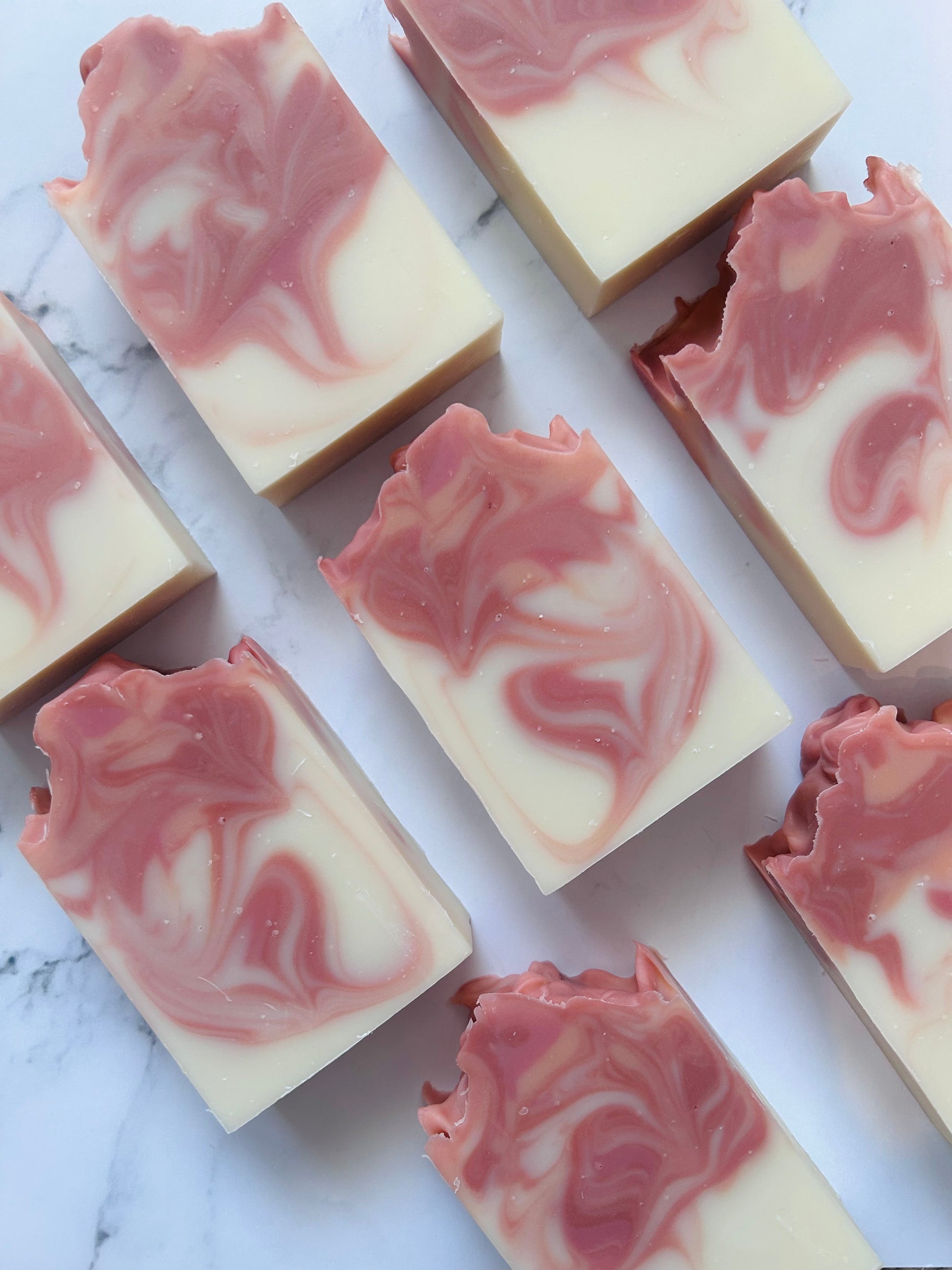 Image of 8 orange and red swirled soap bars photographed vertically on a white marble background.