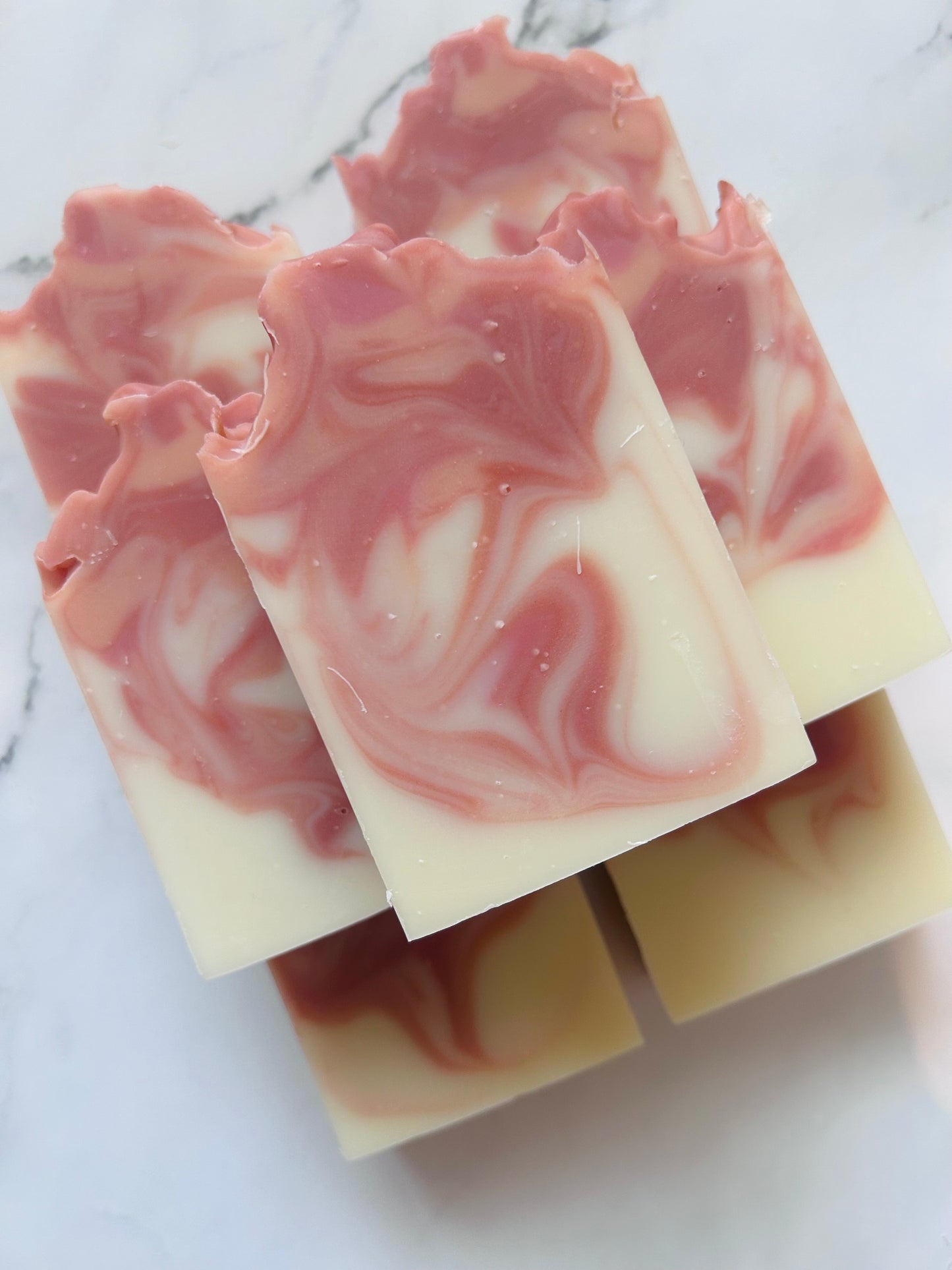 Image of 7 orange and red swirled soap bars stacked on top of one another photographed on a white marble background.