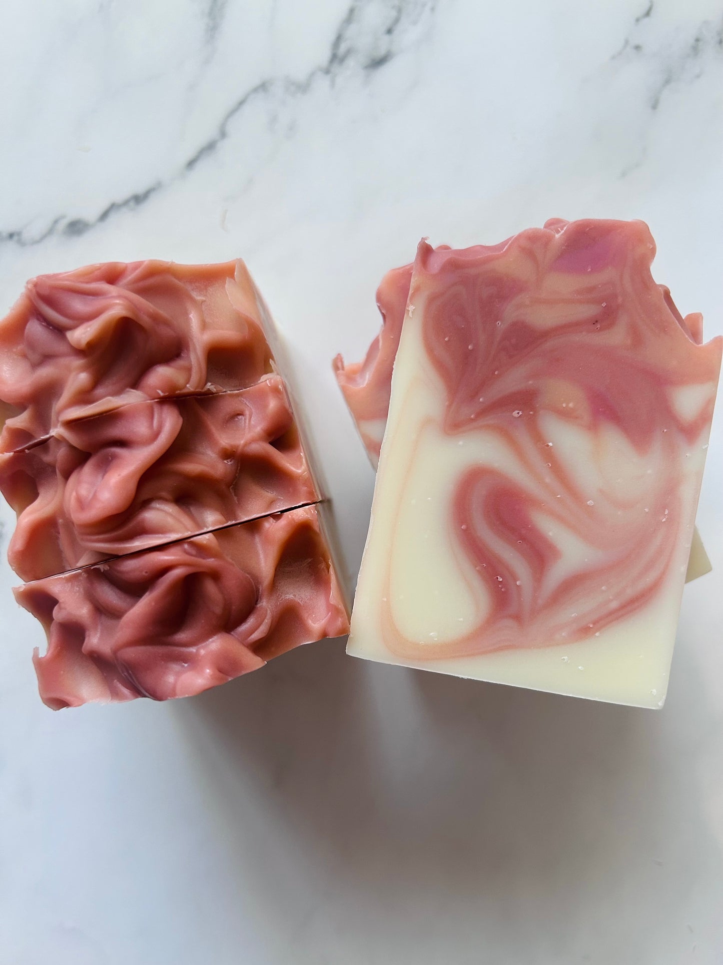 Image of orange and red swirled soap bars with 3 bars stacked on top of one another and 3 bars standing vertically photographed on a white marble background.