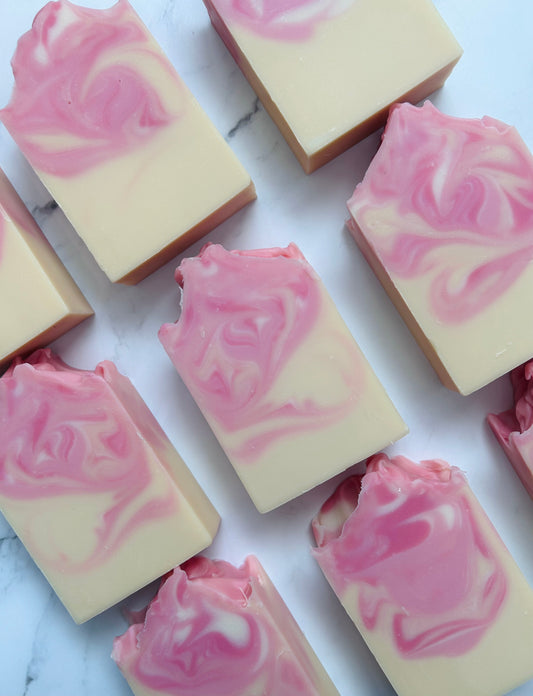 Image of 9 pink, white, and yellow swirled soap bars photographed vertically on a white marble background.
