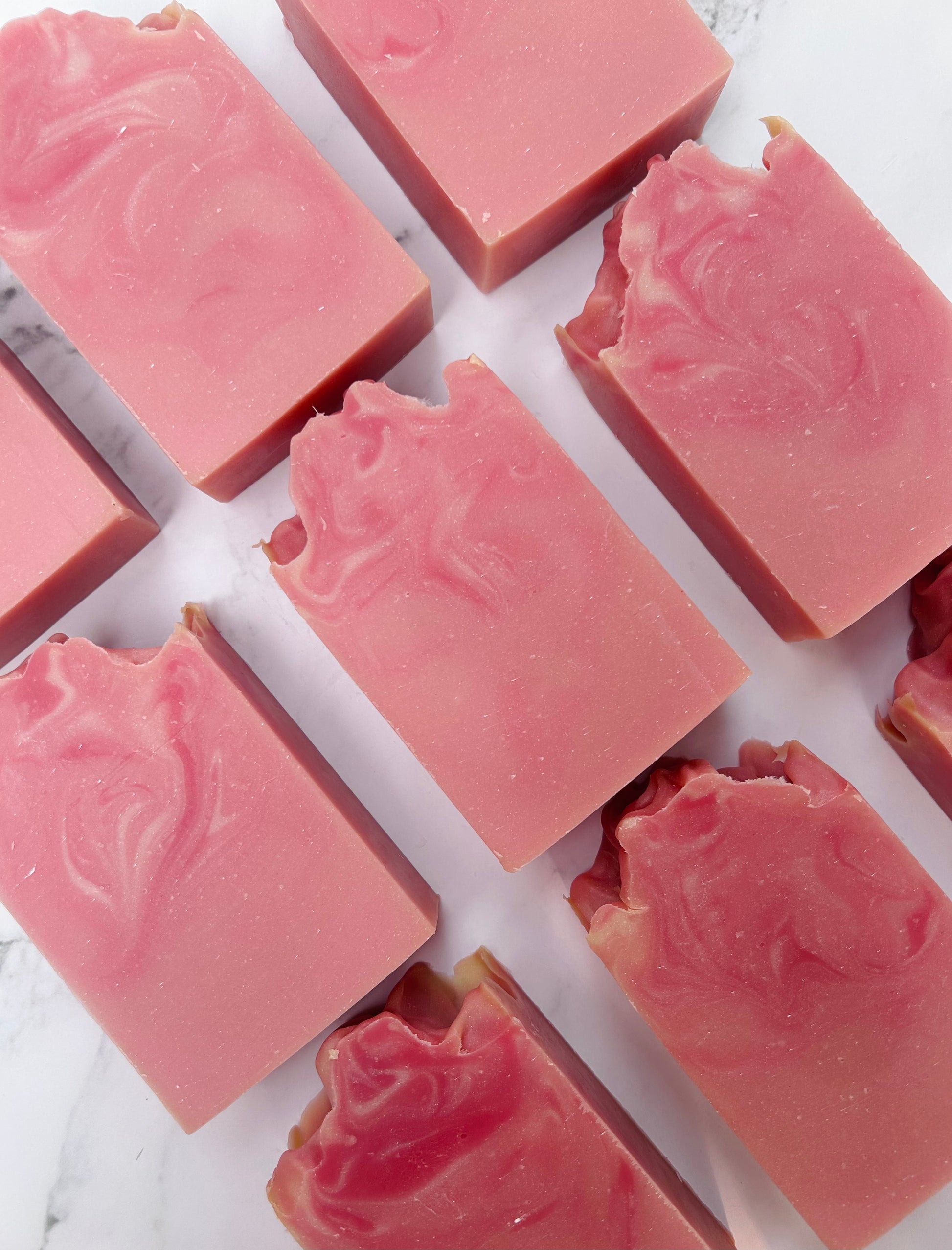 Image of 9 pink and white swirled soap bars photographed vertically on a white marble background.
