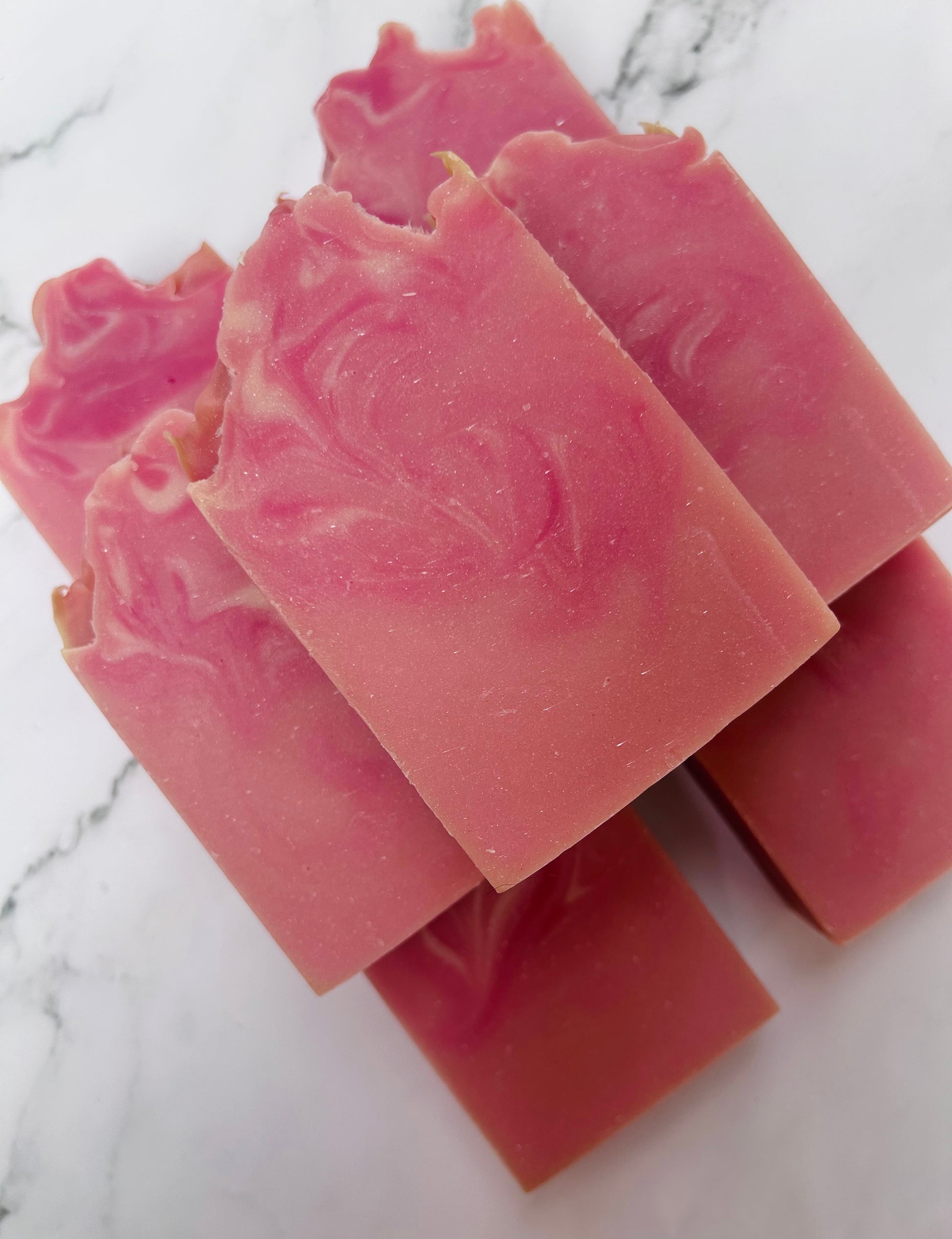 Image of 7 pink and white swirled soap bars stacked on top of one another photographed on a white marble background.