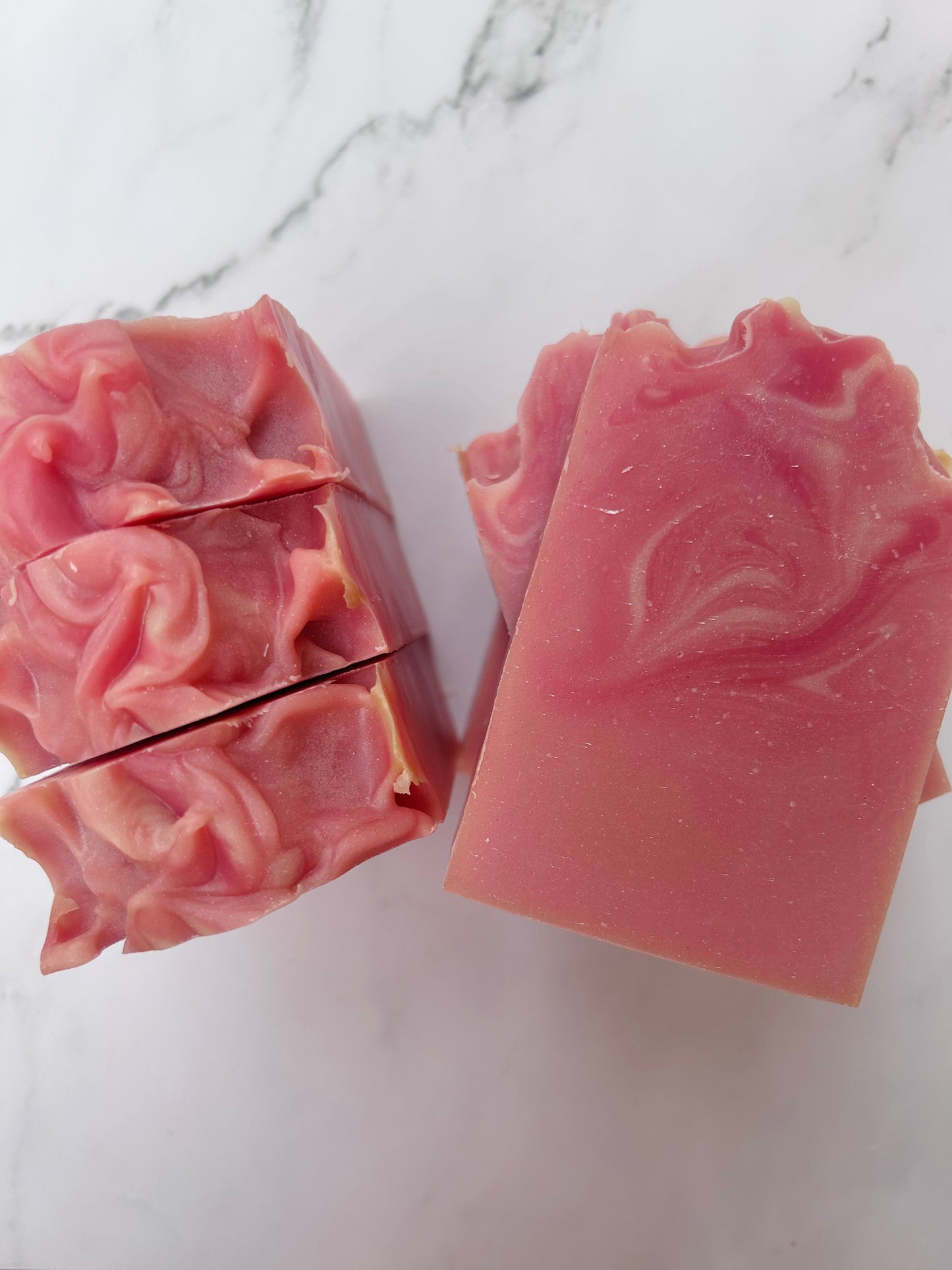 Image of pink and white swirled soap bars with 3 bars stacked on top of one another and 3 bars standing vertically photographed on a white marble background.