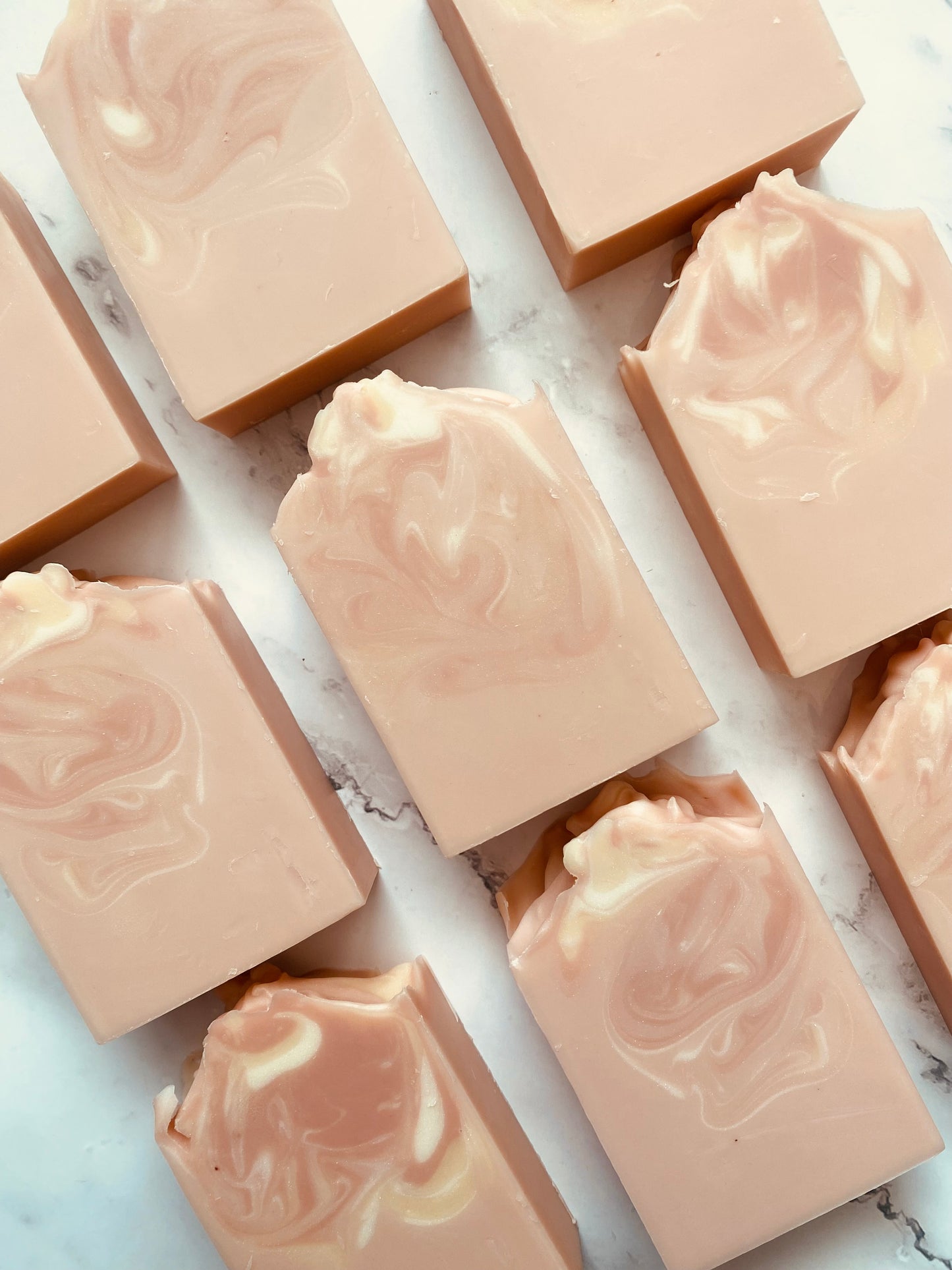 Image of 9 pink and white swirled soap bars photographed vertically on a white marble background.