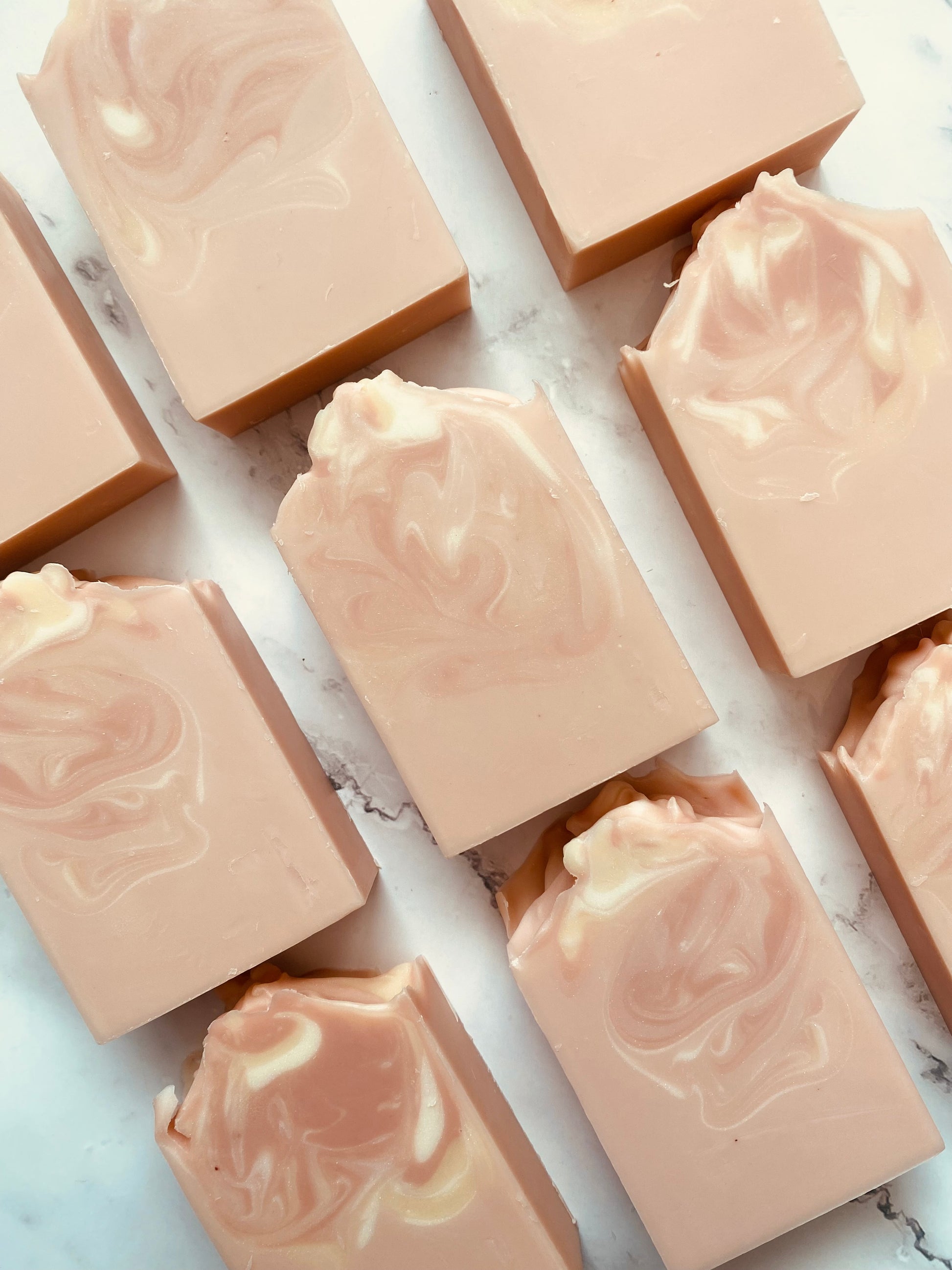 Image of 9 pink and white swirled soap bars photographed vertically on a white marble background.