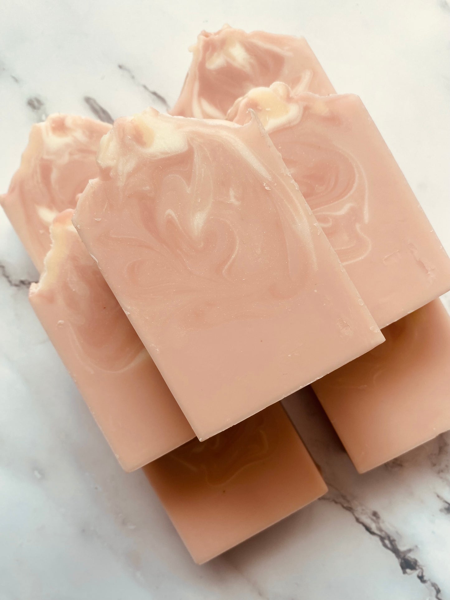Image of 7 pink and white swirled soap bars stacked on top of one another photographed on a white marble background.