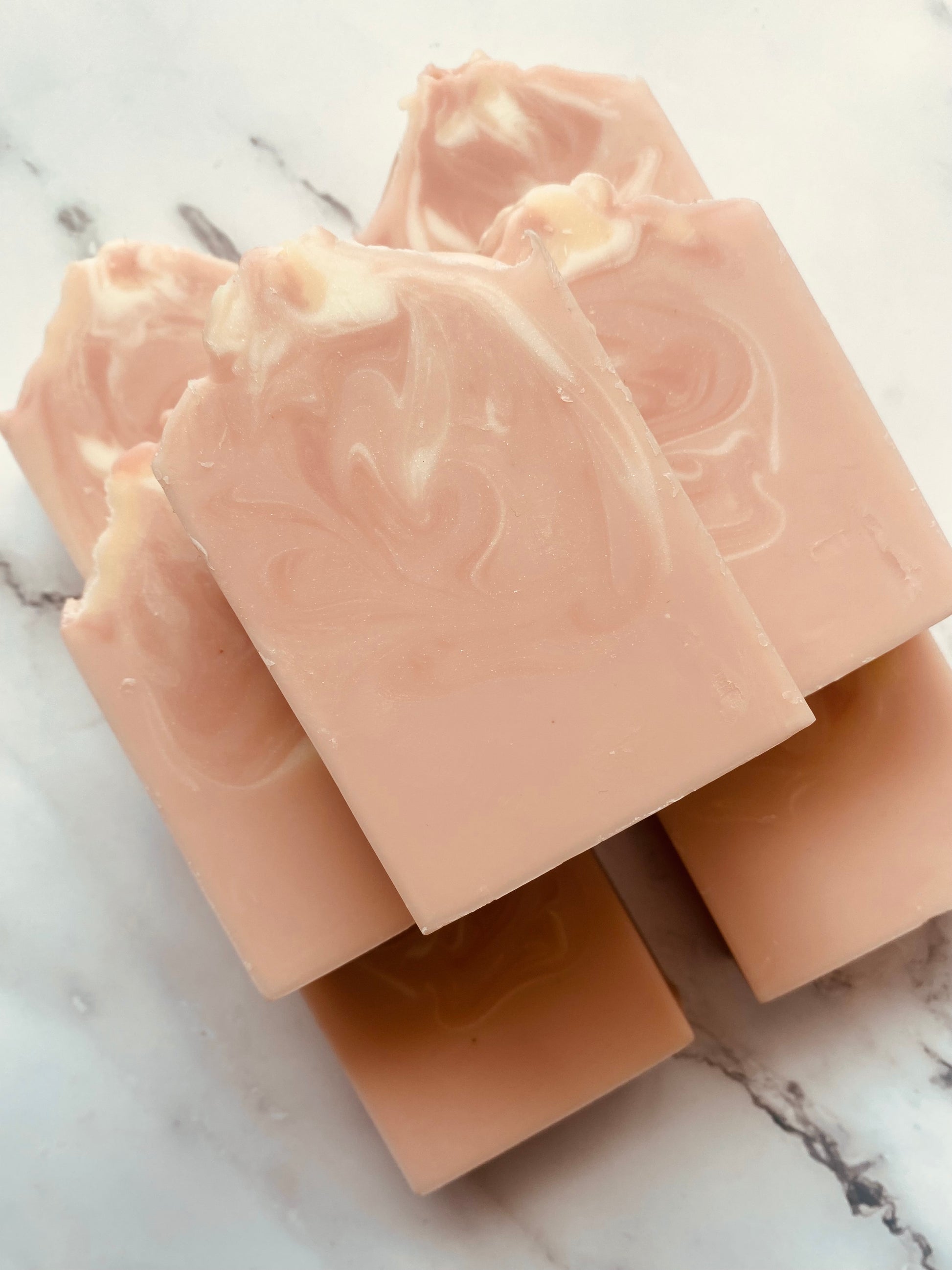 Image of 7 pink and white swirled soap bars stacked on top of one another photographed on a white marble background.