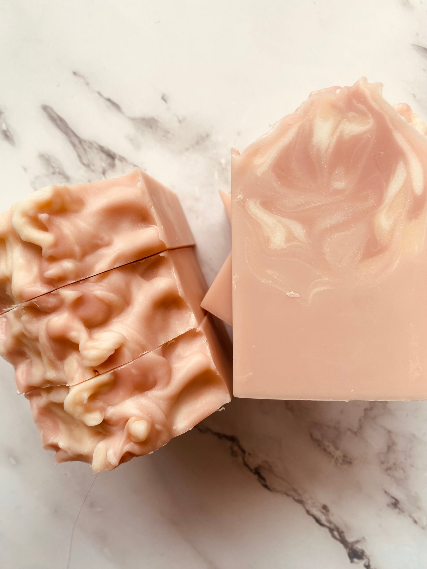 Image of pink and white swirled soap bars with 3 bars stacked on top of one another and 3 bars standing vertically photographed on a white marble background.