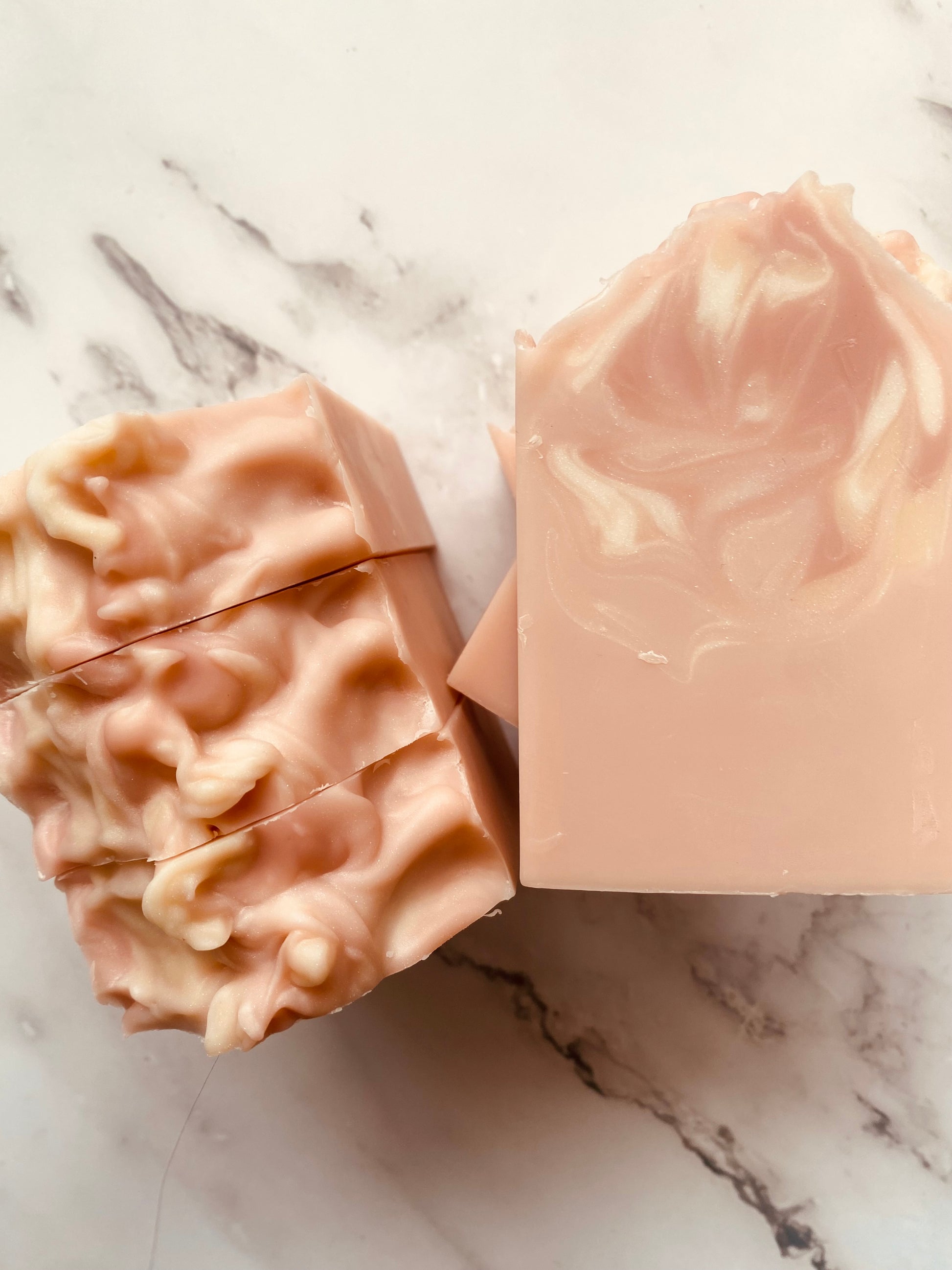 Image of pink and white swirled soap bars with 3 bars stacked on top of one another and 3 bars standing vertically photographed on a white marble background.