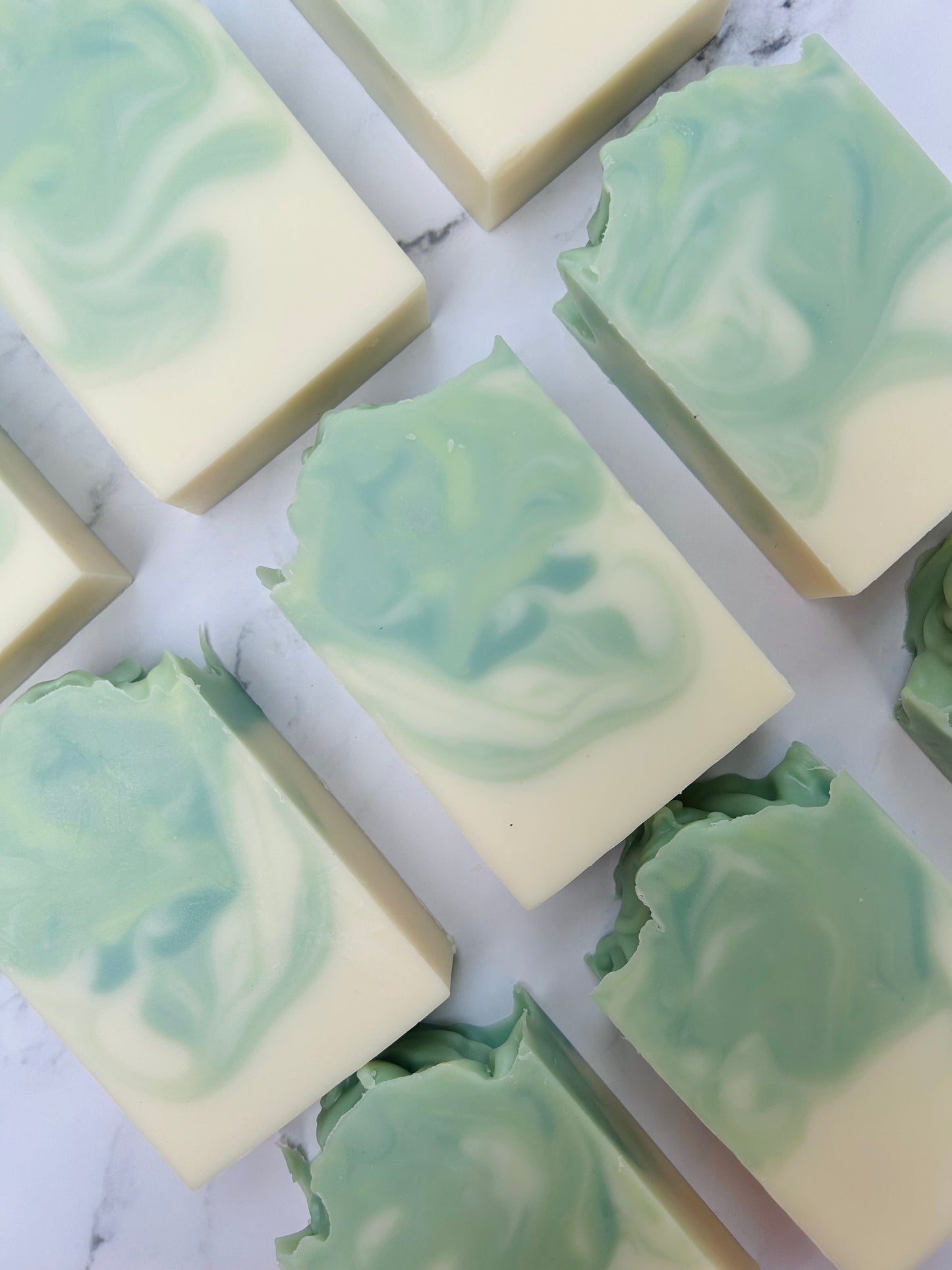 Image of 9 green and white swirled soap bars photographed vertically on a white marble background.
