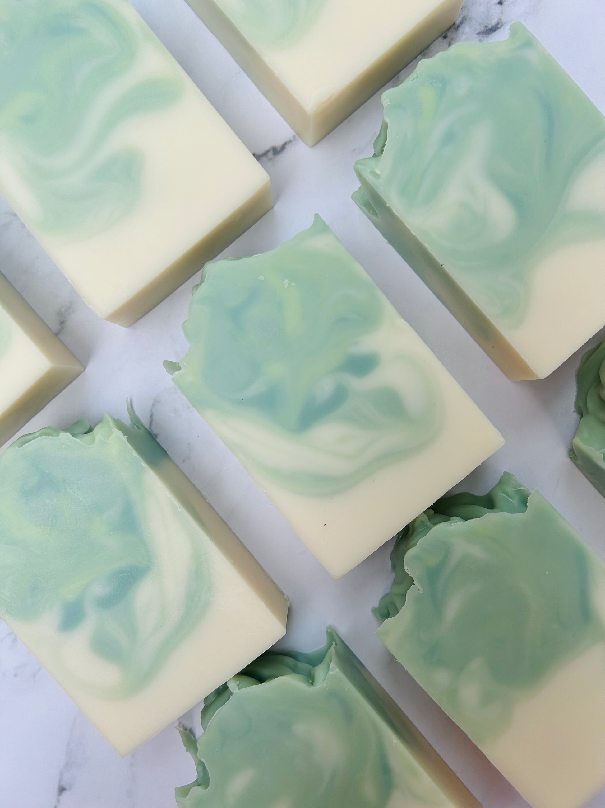 Image of 9 green and white swirled soap bars photographed vertically on a white marble background.