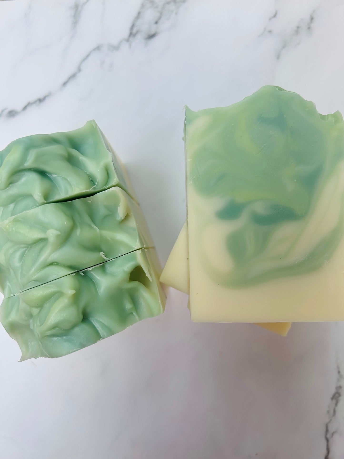 Image of green and white swirled soap bars with 3 bars stacked on top of one another and 3 bars standing vertically photographed on a white marble background.