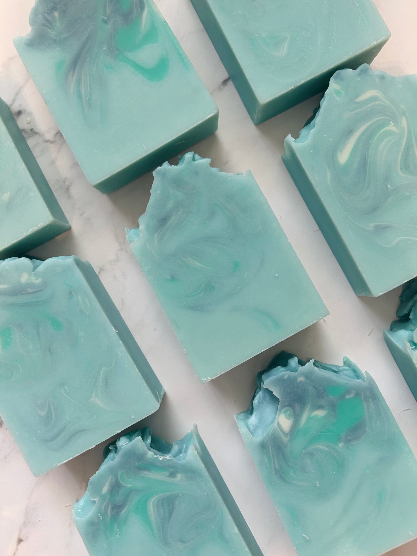 Image of 9 blue, white, and teal swirled soap bars photographed vertically on a white marble background.